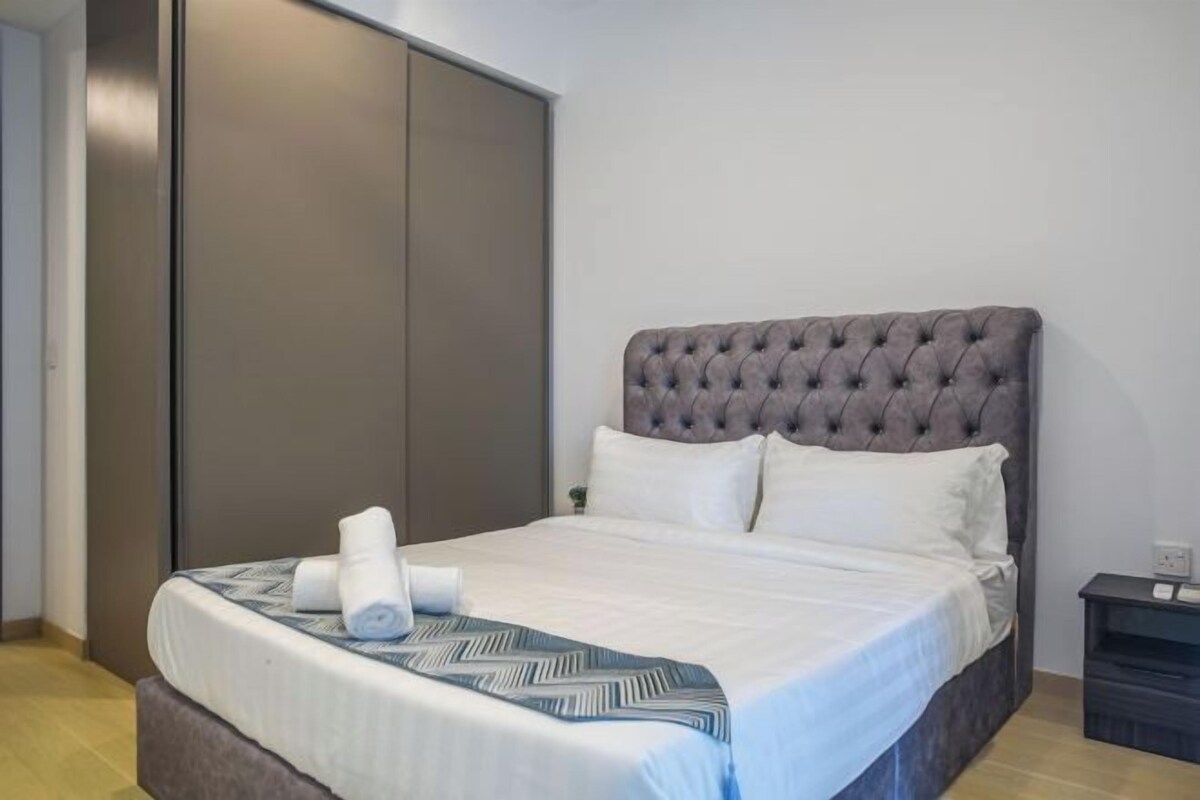 Un lit bien fait, avec une tête de lit capitonnée grise, du linge de lit blanc et un plaid bleu à motifs.