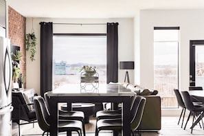 A modern living room with a dining area, large windows, and a city view.
