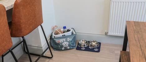 Een eetgedeelte met een houten tafel, twee bruine stoelen, een zak voor diervoeding, twee metalen voerbakken en een marmeren aanrecht.