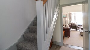 A staircase with a wooden handrail leading to a living room area with a brown leather sofa and a small wooden table. - 9 Station Cottages (Belford)