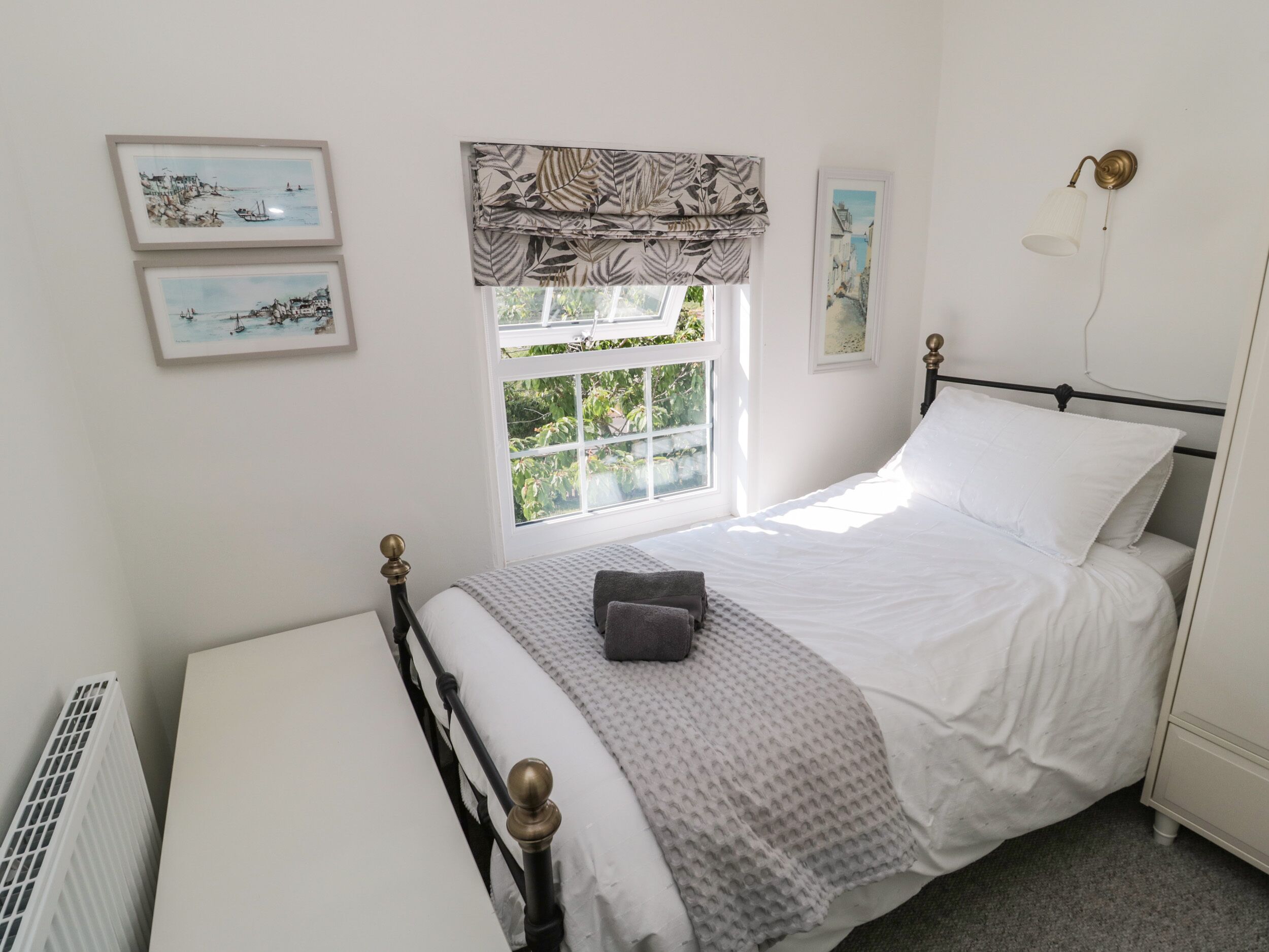 Quarto bem arrumado com cama, radiador, janela com vista e obras de arte nas paredes.