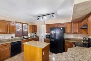 A kitchen with wooden cabinets, a black refrigerator, granite countertops, and a built-in dishwasher. - Glendale w/ Pool & Games (Glendale)