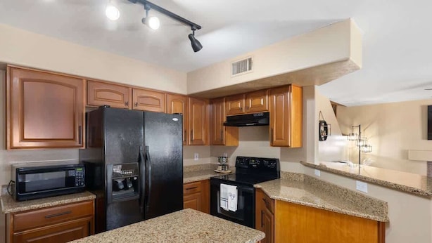 A kitchen with wooden cabinets, a black refrigerator, a microwave, and a stove.