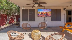 An outdoor patio with wicker furniture, a ceiling fan, and a painting of a canyon.