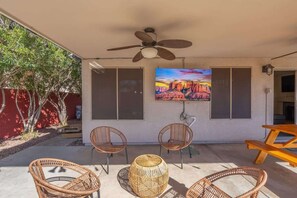 Eine Terrasse im Freien mit Korbmöbeln, einem Deckenventilator und einem Gemälde einer Schlucht.
