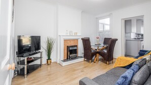 Ein modernes Wohnzimmer mit Flachbildfernseher, Kamin, Essbereich und einer Küche im Hintergrund.