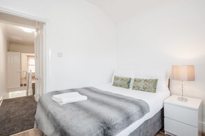 Une chambre à coucher comprenant un lit, une table de chevet, une lampe et une porte donnant sur une autre pièce.