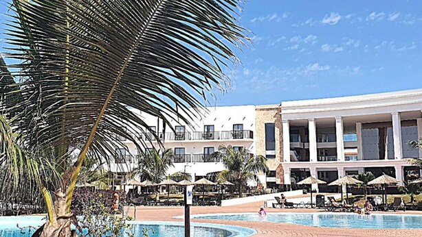 Un resort con piscina, palmeras y un edificio con varios balcones.