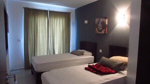 Habitación de hotel con dos camas, un ventanal con cortinas, una obra de arte en la pared y una mesita de noche con lámpara.