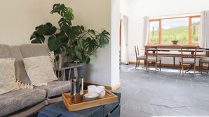 A cozy living room with a sofa, a coffee table with a tray, a large plant, and a dining area with a table and chairs. - Cwmwr (Oswestry)