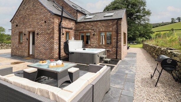 A brick house with a patio area featuring outdoor furniture, a hot tub, and a barbecue grill. - Cwmwr (Oswestry)