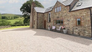 A stone building with a gravel driveway and a view of green hills. - Cwmwr (Oswestry)