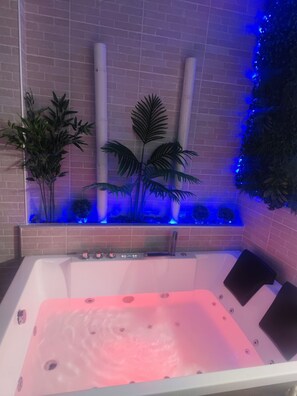 A spa area with a hot tub, a brick wall, and decorative plants.