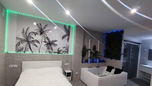 Une chambre à coucher moderne avec un grand lit, une baignoire blanche et une plante fixée au mur.