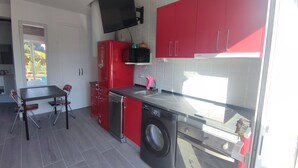 Une cuisine compacte avec des meubles rouges, un lave-vaisselle, une machine à laver et un téléviseur à écran plat fixé au mur.