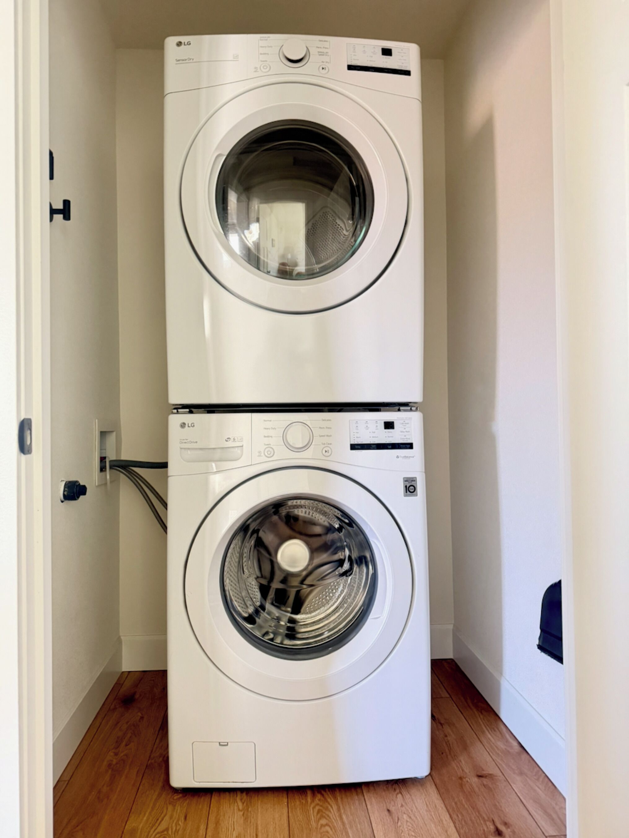 A stacked washer and dryer unit in a hallway with wooden flooring.