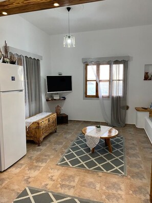 A compact kitchen with a refrigerator, a television, a wooden chest, and a dining table with a lace tablecloth.