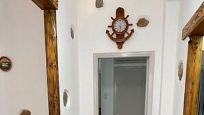 Een modern interieur met een houten accentmuur, een klok, een bank met kussens, een vaas met gedroogde planten en een vloerkleed met dessin.