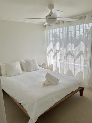 Relax in a spacious bedroom with a large bed, ceiling fan, and window with sheer curtains.