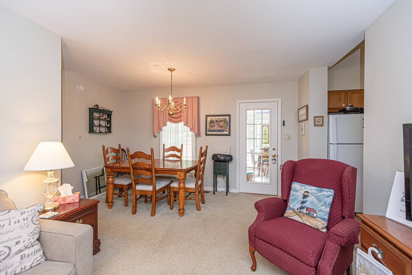 A dining area with a wooden table and chairs, a red armchair, a lamp, and a door leading to a kitchen.
