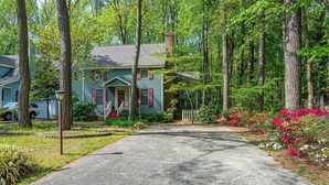 A two-story house with a front porch, surrounded by a wooded area and a driveway leading to the front door. - Coastal Colonial Charm located in Ocean Pines, MD by Karsons Keys (Ocean Pines)