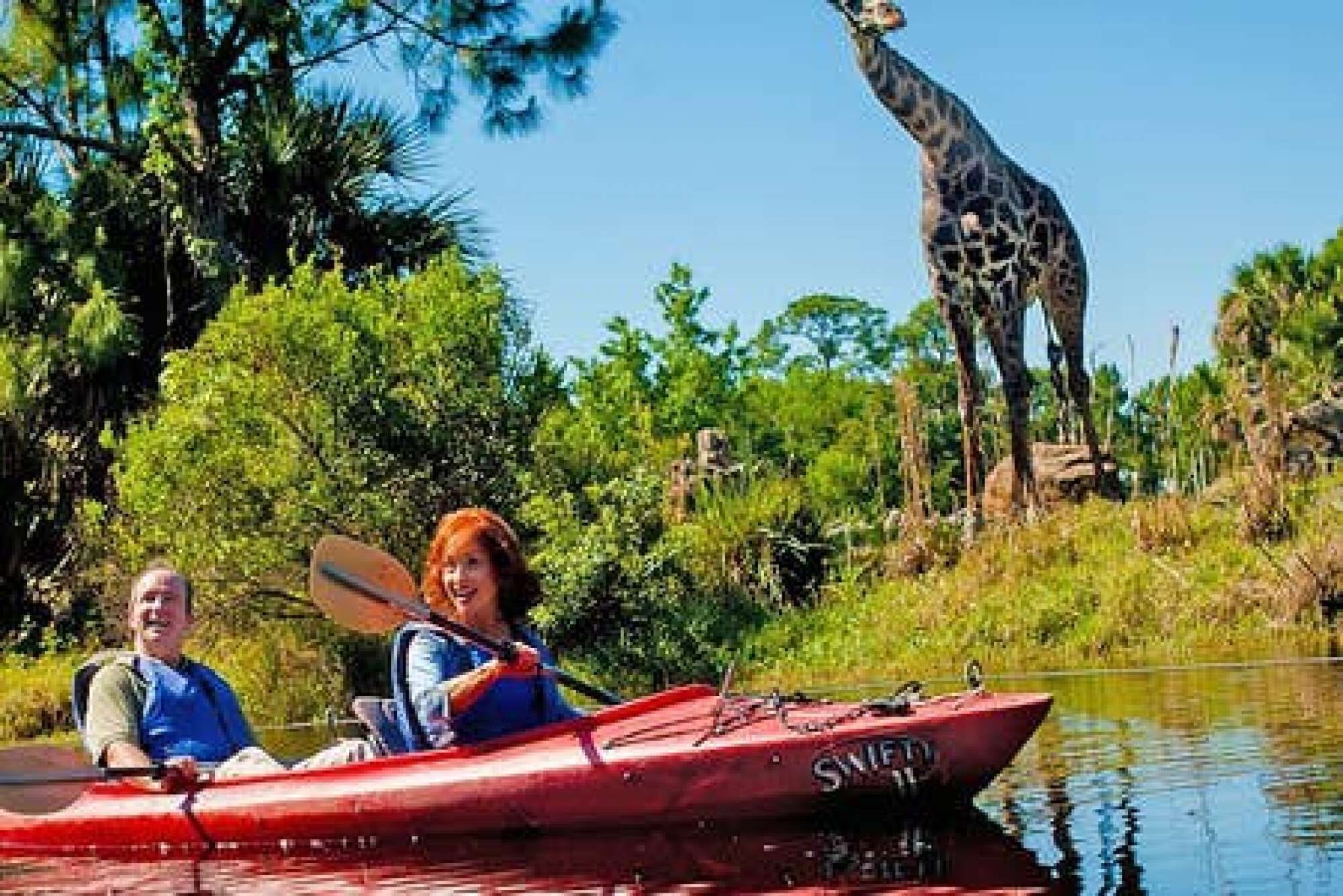 Un kayak rojo con la inscripción "SNIF", una persona remando y una jirafa al fondo.