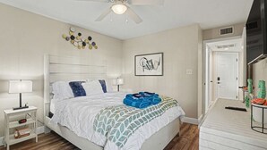 Un dormitorio con cama, mesitas de noche, ventilador de techo, decoración en la pared y una puerta.