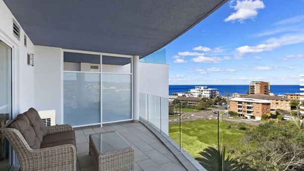 A balcony with wicker furniture, a glass door, and a view of buildings and the ocean.