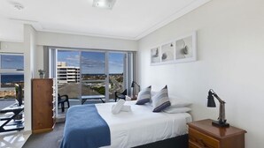 A bedroom with a bed, bedside table, lamp, and a view of the city through large windows.