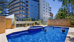 A swimming pool with a curved edge, surrounded by a brick wall and potted plants.
