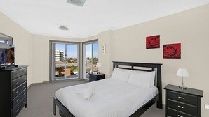 A bedroom with a bed, two bedside tables, a dresser, and a television.