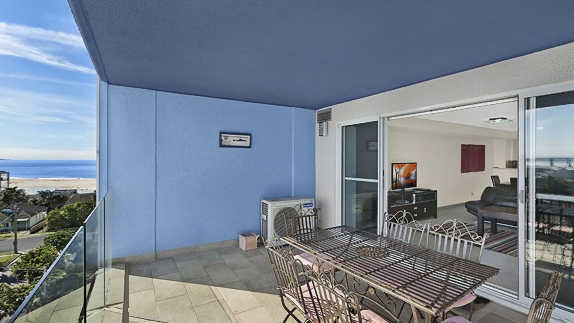 Un balcon avec une table et des chaises, une porte-fenêtre coulissante donnant sur un espace de vie et une vue sur la plage.