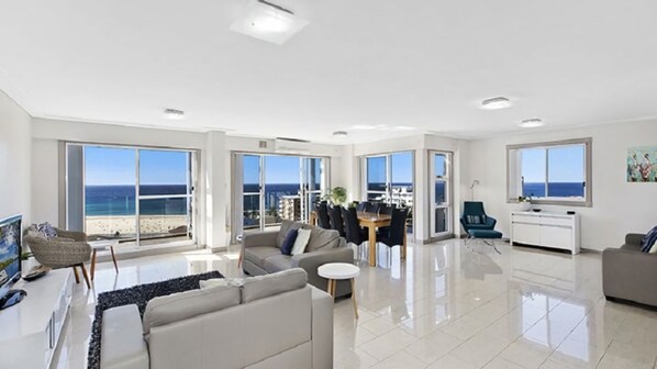 A spacious living room with a large window overlooking the beach, a dining area with a view, and a modern kitchen.
