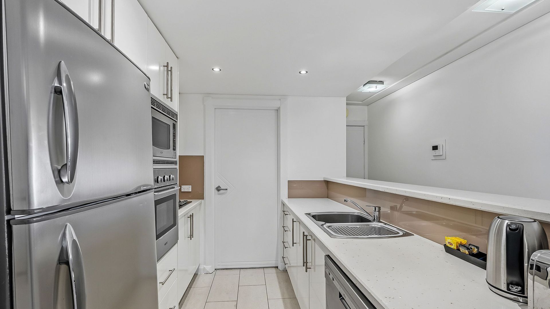 A compact kitchen with stainless steel appliances, a white countertop, and a single sink.