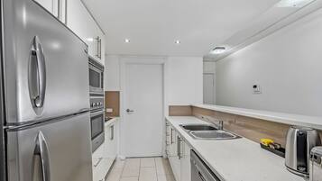 A compact kitchen with stainless steel appliances, a white countertop, and a single sink.