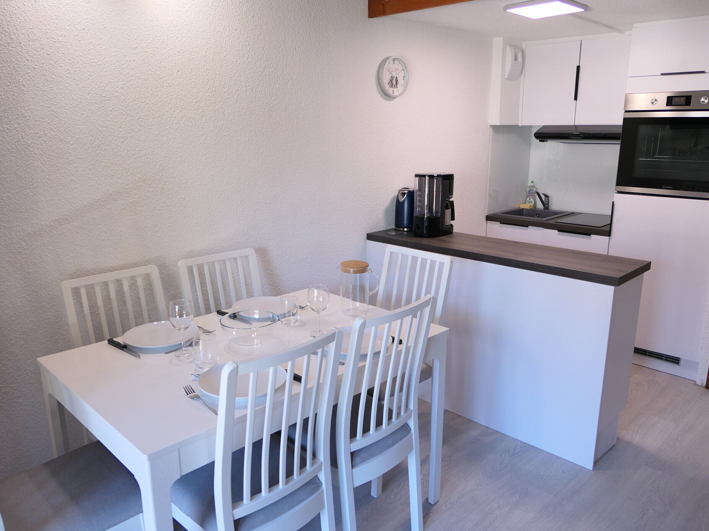 Una cocina moderna con armarios blancos, horno empotrado y cafetera sobre la encimera.