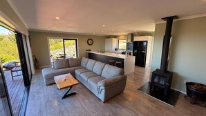 A modern living room with a sectional sofa, a wooden coffee table, and a fireplace. - Golden Bay Heights - Luxury Accommodation (Parapara)