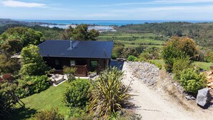 A modern house with a dark roof, surrounded by lush greenery and a view of the ocean. - Golden Bay Heights - Luxury Accommodation (Parapara)