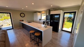 A modern kitchen with a central island, bar stools, a built-in oven, and a large window. - Golden Bay Heights - Luxury Accommodation (Parapara)