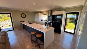 A modern kitchen with a central island, bar stools, a built-in oven, and a large window. - Golden Bay Heights - Luxury Accommodation (Parapara)