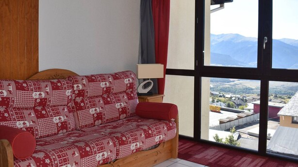 A wooden sofa with a red and white patterned cover, a lamp, and a view of a mountainous landscape through large windows.