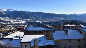 A residential area with snow-covered roofs and houses, set against a backdrop of snow-capped mountains under a clear blue sky.