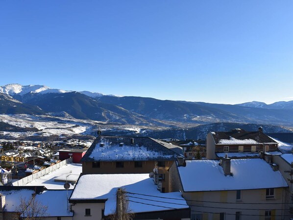 A residential area with snow-covered roofs and houses, set against a backdrop of snow-capped mountains under a clear blue sky.