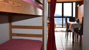 A bunk bed with a red mattress, a wooden headboard, and a view of a dining area with a table and chairs.