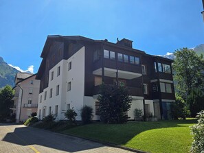 A multi-story building with balconies, a driveway, and a mountain backdrop.