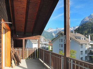 A wooden balcony with a view of snow-capped mountains and residential buildings. - Dorfstrasse 53a / 2 Appartement/Fewo 6-Bettwohnung by Interhome (Engelberg)
