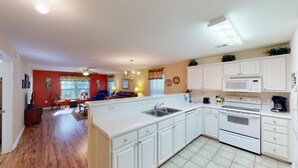 A modern kitchen with white cabinetry, a central island, and a dining area with a red wall and wooden flooring. - Pawleys Island Fairway Retreat 3BR Villa (Pawleys Island)
