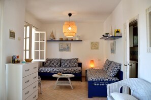 A cozy living room with a sofa, a chair, a small table, and a hanging light fixture. - Spacious and bright apartment near the beach (Capoliveri)