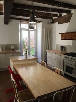 A kitchen with a wooden table, red chairs, a stove, and a window with a view of greenery.