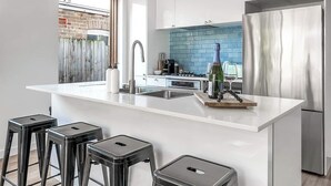 A modern kitchen with a white island, stainless steel appliances, and black bar stools.